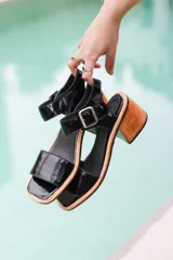 Sandalias negras de cuero charol, con tira ancha sobre los dedos y tobillo con hebilla metálica. Taco de madera.