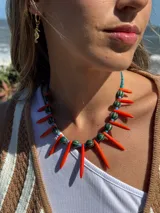 Collar corto con cuentas de cerámica verde y azul, pinchos de piedra reconstituida color naranja y detalles de cristales checos y mostacillas. Se cierra con cadena de acero quirúrgico para regular el largo.