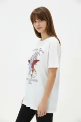 Remera de algodón negra de manga corta y cuello redondo, con estampa frontal que incluye letras rojas y gráficos en tonos dorados.