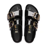 Sandalia Birkenstock modelo Arizona con dos correas anchas de cuero charolado negro y hebillas grandes metálicas doradas. Cuenta con plantilla anatómica de corcho y suela de goma antideslizante.