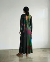 Vestido largo de corte recto y silueta fluida, confeccionado en jersey suave. Presenta un diseño de manga larga, cuello redondo y una estampa abstracta con trazos verticales en tonos oscuros, azules, verdes y rojizos.