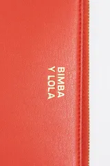 Billetera de estructura rígida Bimba y Lola, color naranja, con cierre de cremallera y tirador de cordón. Presenta el logo de la marca grabado en dorado en el frente.