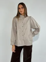 Camisa color beige con cuello mao, mangas largas abullonadas y cierre frontal con botones.