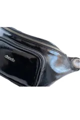 Riñonera de charol negro, con diseño estructurado, bolsillos frontales con cierre y herrajes metálicos plateados.