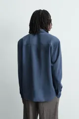 Camisa de corte relajado confeccionada en tejido con mezcla de viscosa. Presenta cuello solapa, manga larga con puños abotonados, bolsillos de plastrón con solapa en el pecho y cierre frontal de botones.