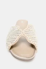 Sandalia plana tipo pala de color beige, con tira ancha decorada con perlas y abalorios brillantes dispuestos en patrón radial, punta redonda y suela plana.