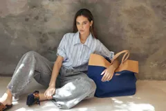 Camisa de corte recto y relajado, con cuello clásico, mangas cortas con detalle de ajuste y cierre frontal con botones. Presenta un diseño de rayas verticales en tonos celestes, blancos y grises.