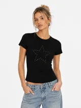 Remera tipo baby tee de color negro, con ajuste al cuerpo y mangas cortas. Presenta un diseño de estrella formado por pequeñas tachas metálicas en la parte frontal.