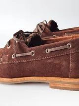 Sandalias de cuero gamuzado color marrón chocolate, diseño tipo huarache con tiras entrelazadas, tira en el empeine, talón cerrado y hebilla metálica de ajuste lateral.