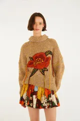 Sweater tejido color mostaza con cuello alto, mangas largas y un gran bordado floral en el frente con detalles colgantes.