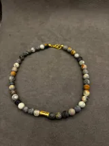 Collar corto de piedras volcánicas marrones y marrones oscuras, con detalle cilíndrico dorado en el centro.