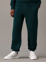 Pantalón de chándal verde oscuro de felpa gruesa con cintura y puños elásticos, bolsillos laterales y traseros, corte recto y holgado. Con bordado de Calvin Klein en la cadera.