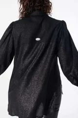Camisa negra holgada con efecto brillante, frunces en las mangas, puños anchos y largo por debajo de la cola. Incluye un bordado del logo en la espalda.