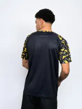 Remera deportiva de hombre, color negro, con cuello redondo y mangas cortas con estampado geométrico en amarillo y gris. Lleva el escudo de Peñarol en el pecho.