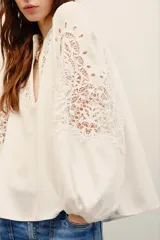 Camisa blanca de manga larga con detalles de encaje guipure en el pecho y las mangas, cuello en V y corte holgado.