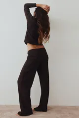 Pijama de dos piezas en punto acanalado color marrón oscuro. Incluye remera de manga larga con cuello redondo y detalle de aplique floral en el centro, y pantalón largo de corte recto con cintura elástica.