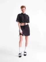 Camisa crop negra de tencel, con mangas cortas y detalles de encaje en el cuello, la botonera frontal, el dobladillo inferior y las mangas. Cuenta con tiras ajustables que se atan alrededor de la cintura.