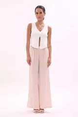 Pantalón largo de tiro alto, color rosa pálido, de corte ancho y fluido. Presenta una hilera de recortes ovalados decorativos a lo largo de la costura lateral.