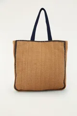 Bolso tote de mano color tostado, tejido con textura tipo mimbre o rafia, con bordes y detalles en azul marino. Cuenta con un asa superior corta, cierre con cremallera y un bordado frontal con la palabra "Rio" que incluye motivos tropicales de una palmera y un tucán.
