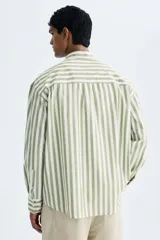 Camisa de popelina de algodón con cuello inglés, tapeta clásica, bolsillo superior abierto y canesú con pliegue en la espalda. Cuenta con mangas largas, puños ajustables con botón y bajo ligeramente redondeado. Presenta un diseño de rayas verticales en tonos verde y blanco.