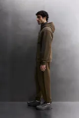 Pantalón jogger de entrenamiento, corte regular fit, color verde oliva oscuro. Confeccionado en tejido técnico compacto de algodón con elasticidad y efecto neopreno. Presenta cintura elástica ajustable con cordón blanco, bolsillos frontales y un bolsillo lateral con cierre de cremallera. El bajo termina en puño.