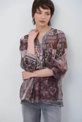 Camisa de corte recto con cuello mao y cierre frontal parcial de botones. Presenta un diseño estampado tipo patchwork con motivos florales y geométricos en tonos tierra, marrones y beige. Posee mangas tres cuartos con puños simples.