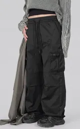 Pantalón cargo de corte regular confeccionado en textil técnico pesado. Presenta cintura elástica con cordón de ajuste, bolsillos laterales en la cintura y bolsillos cargo de gran tamaño en los muslos. Incluye elásticos con tancas en los tobillos para regular la apertura de la pierna.