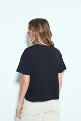 Remera blanca de manga corta con estampa frontal de un personaje con lentes de sol y la frase "Llegué tarde porque no quería venir". Tiene silueta relajada y calce cómodo, con un corte asimétrico en el bajo.