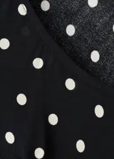 Vestido largo negro con estampado de lunares blancos, de corte recto, escote redondo y mangas largas.