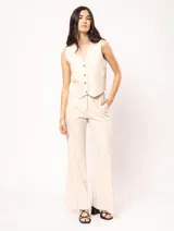 Pantalón de lino color beige, de tiro alto, pierna ancha y levemente acampanada. Tiene pinzas delanteras, elástico en la pretina trasera, cierre delantero y broche interno, bolsillos laterales y dobladillo invisible.