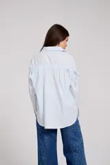 Camisa blanca de corte holgado con cuello camisero y cierre frontal de botones. Presenta un delicado bordado vertical de flores pequeñas en color bordó a lo largo de la botonera y en el cuello.