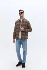 Camisa de manga larga confeccionada en viyela de algodón con diseño de cuadros en tonos marrones. Presenta cuello clásico, cierre frontal con botones y un bolsillo aplicado en el pecho.
