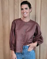 Camisa de color marrón con cuello redondo, cierre frontal con botones y mangas largas abullonadas con puños elásticos.