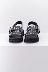 Sandalia de cuero color marrón con suela track negra. Presenta dos tiras frontales con ojalillos metálicos y una tira trasera con cierre de velcro.