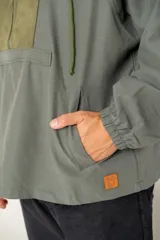 Canguro tipo anorak de color verde militar, con capucha ajustable y cierre frontal parcial. Presenta un panel central en contraste de textura gamuzada y un bolsillo frontal tipo canguro con solapa.