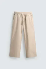 Pantalón relaxed fit color beige con rayas verticales finas, confeccionado en tejido de algodón. Cuenta con cintura elástica ajustable con cordón, bolsillos frontales y bolsillos traseros de plastrón.