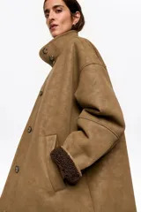 Chaquetón de corte recto en piel sintética color tostado, con botones frontales, cuello subido, manga larga recta y bolsillos de vivo. Presenta un interior forrado en pelo sintético.