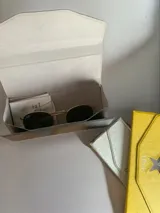 Estuche para lentes plegable con diseño rígido y cierre magnético. Presenta una estrella metálica decorativa en la solapa frontal y el logo de la marca estampado. El interior está forrado en material suave para proteger los cristales.