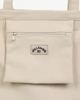 Tote bag Billabong de lona color beige con diseño estampado de la colaboración con Ty Williams que muestra figuras cargando una tabla de surf y un sol rosado.