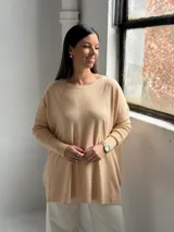 Sweater de punto color beige, de corte holgado y diseño asimétrico con tajos laterales. Presenta cuello redondo y mangas largas con puños acanalados, además de un detalle de costura vertical central.
