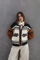 Campera tipo bomber tejida en lana merino, con diseño artesanal que combina guardas estilo patagónicas y detalles de flores bordadas. Presenta cierre frontal y terminaciones en tejido acanalado.