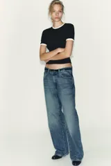 Camiseta blanca de manga corta y cuello redondo, con ribete negro decorado con perlas blancas en el cuello y los puños.