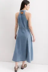 Vestido midi de denim celeste, con cuello camisero halter, botones dorados en el frente, bolsillos en el pecho y falda acampanada.
