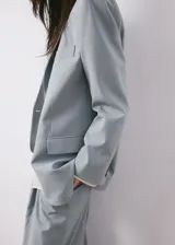 Blazer de corte recto color celeste, con solapa de muesca, cierre frontal con un botón negro y bolsillos con solapa.