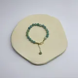 Pulsera de cuentas de amazonita de 6 mm de diámetro, con separadores de hilo color verde agua y cierre con piezas metálicas bañadas en oro. Incluye una cadena de alargue con un dije de piedra natural colgante.