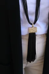 Collar largo de múltiples hilos negros con dije rectangular de textura rugosa en tono dorado y fleco largo de hilos negros colgante.