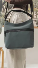 Cartera tipo hobo de tamaño grande en color beige, con detalles en negro. Presenta una franja horizontal negra con el logo de la marca, asa corta de hombro y correa larga desmontable. Incluye bolsillo frontal con cierre oculto y bolsillo trasero.