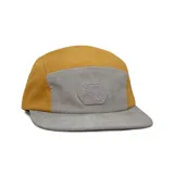 Gorra tipo 5-panel con diseño bicolor que combina paneles laterales en color mostaza y panel frontal y visera en color gris. Presenta un parche frontal de goma con diseño topográfico y logo de la marca. Fabricada con materiales reciclados.