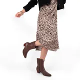 Bota corta de cuero color marrón, con taco cuadrado y punta fina. Presenta una correa con tachas pequeñas y una argolla metálica decorativa alrededor del tobillo. Cuenta con cierre lateral.