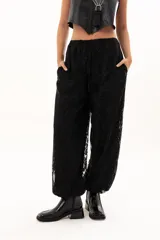 Pantalón de encaje negro con diseño floral, corte holgado y cintura elástica con cordón ajustable. Cuenta con bolsillos laterales.